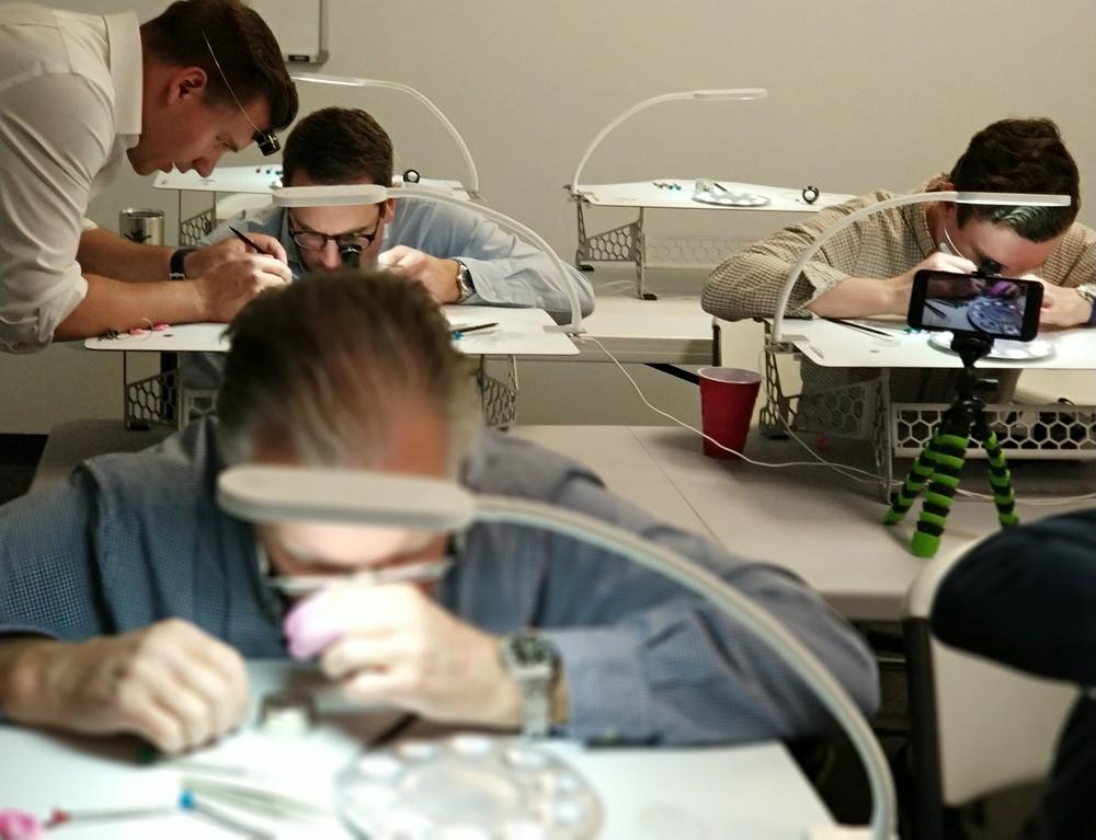 An instructor helps a participant while others work at their benches