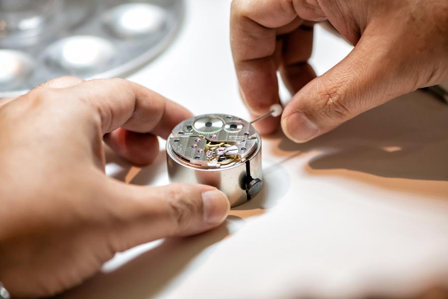 Close-up of hands steadying a movement holder while working on a hand-wound movement