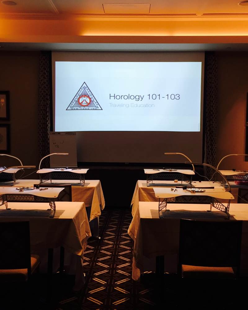 A private room set up in classroom format with lamps, benches and a projection screen showing Horology 101-103