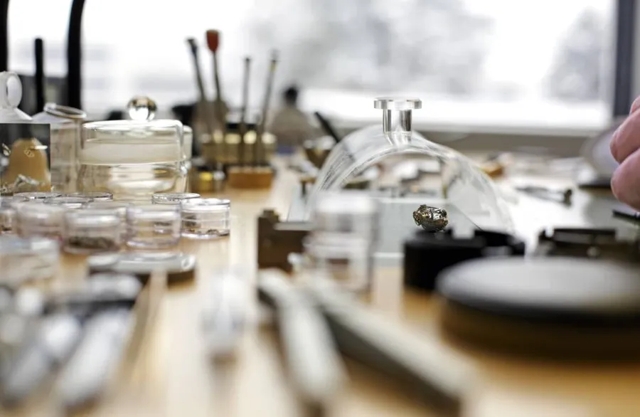 A watchmaker's bench with tools, parts boxes and a movement under a dust cover, in soft focus