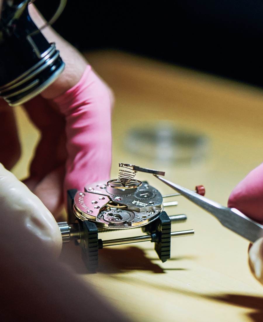 A student holds tweezers over a mechanical watch movement on a bench