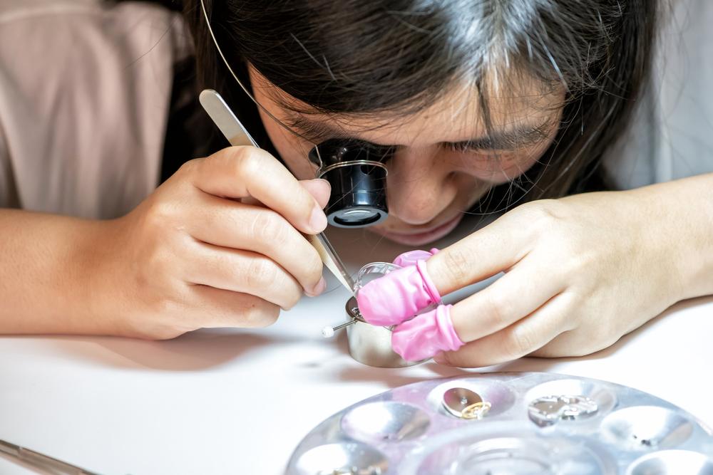 A participant with a loupe uses tweezers on a movement