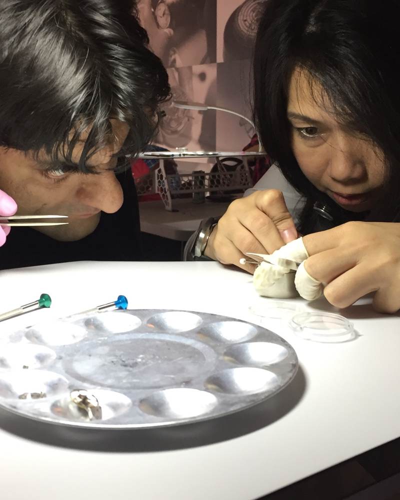 Two students lean over a watchmaking bench with a parts tray and movement holder