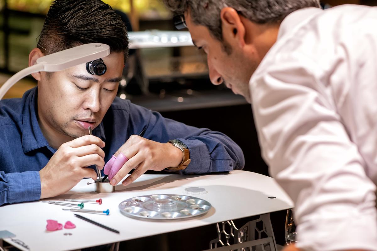 The instructor leans in beside a participant who wears a loupe on his forehead