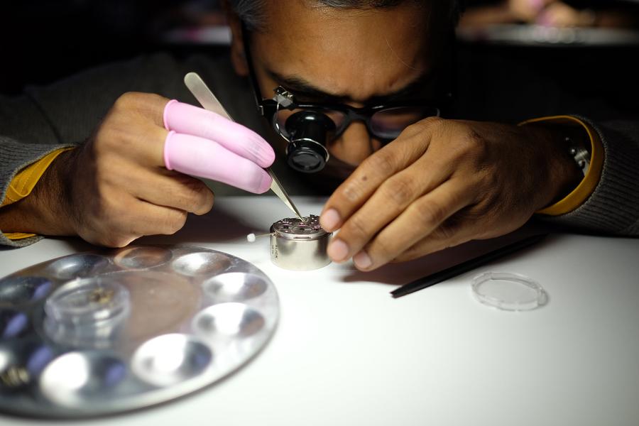 A participant wearing glasses and a loupe works on a movement with tweezers
