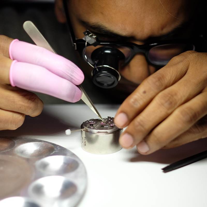 A student with a loupe and finger cots holds tweezers above a movement