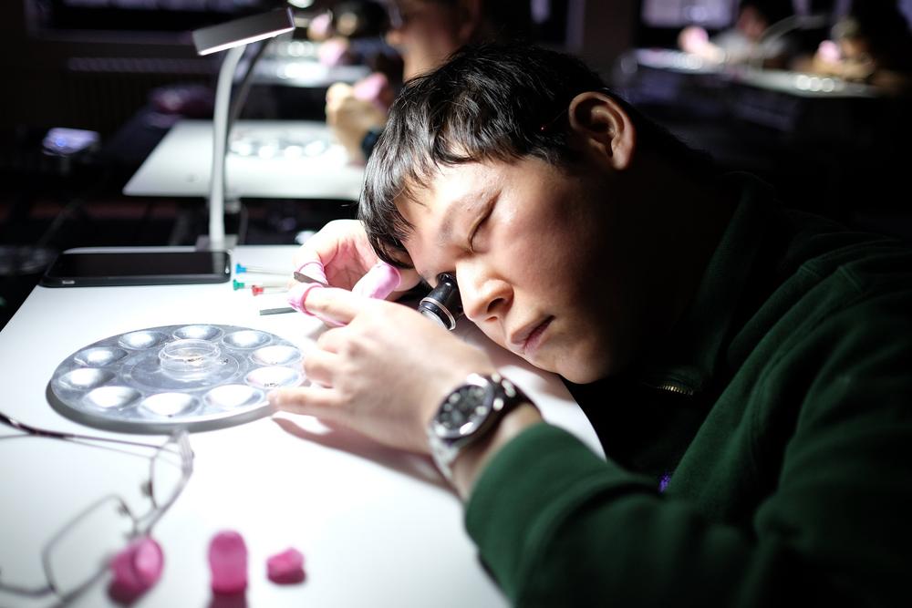A participant with a loupe concentrates on his movement under the bench lamp